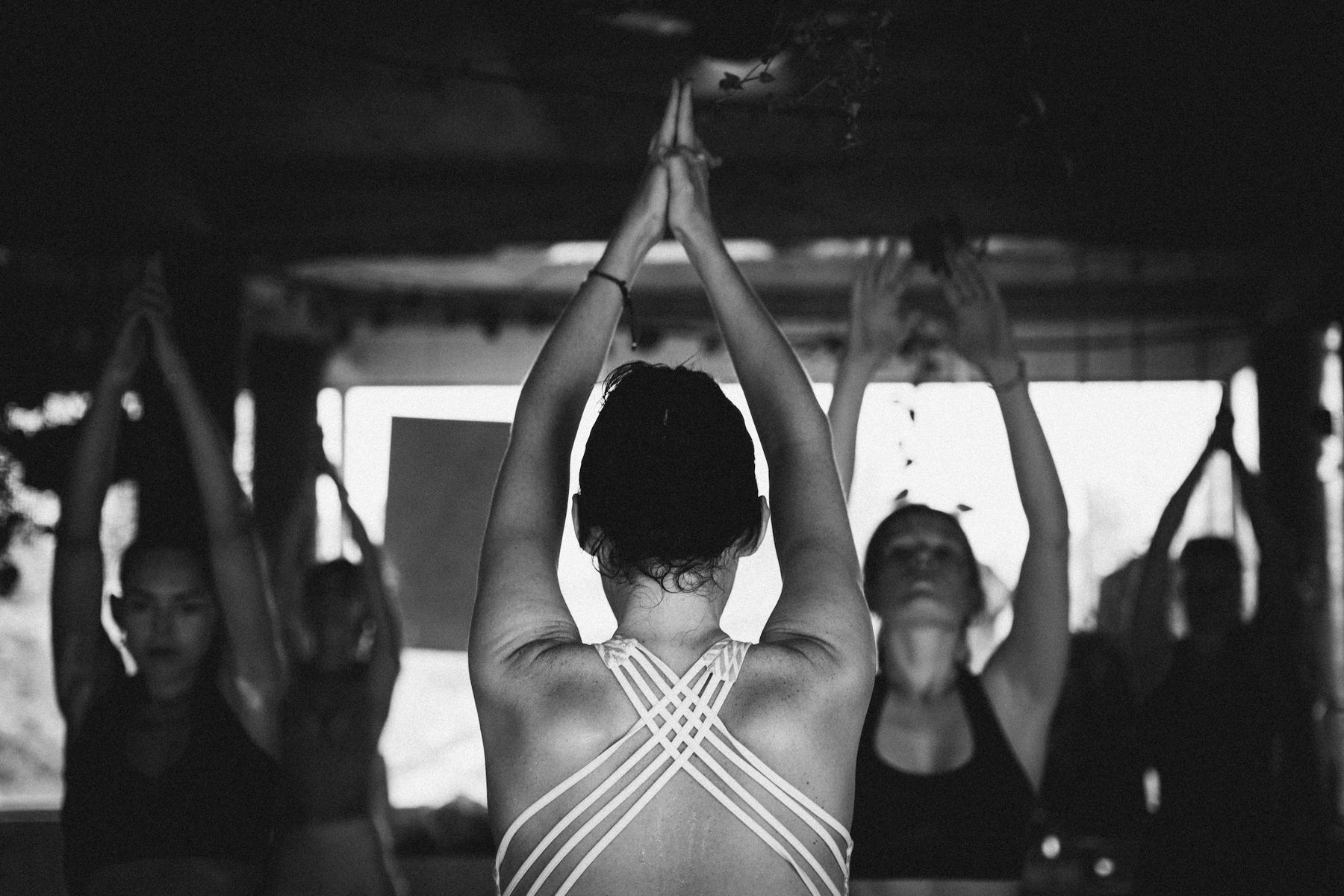 Photo en noir et blanc : une élève, mains jointes au-dessus de la tête, face au groupe